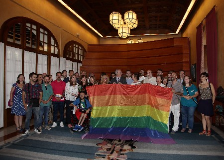 El presidente del Parlamento, diputados y representantes de colectivos LGTBI posan con la bandera de la diversidad en el Salón de Protocolo